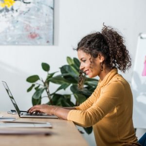 Steps to Promote a Wellness Workshop - Whole Family Coaching. Woman sitting at a desk typing on a laptop.